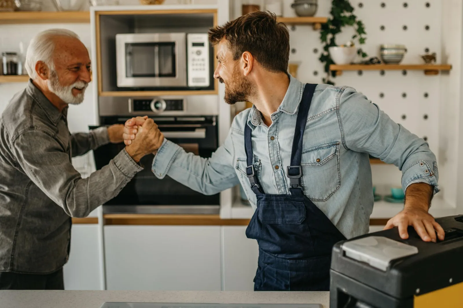 Two neighbors clasping hands warmly — a tradesman with his toolbox helping out at home