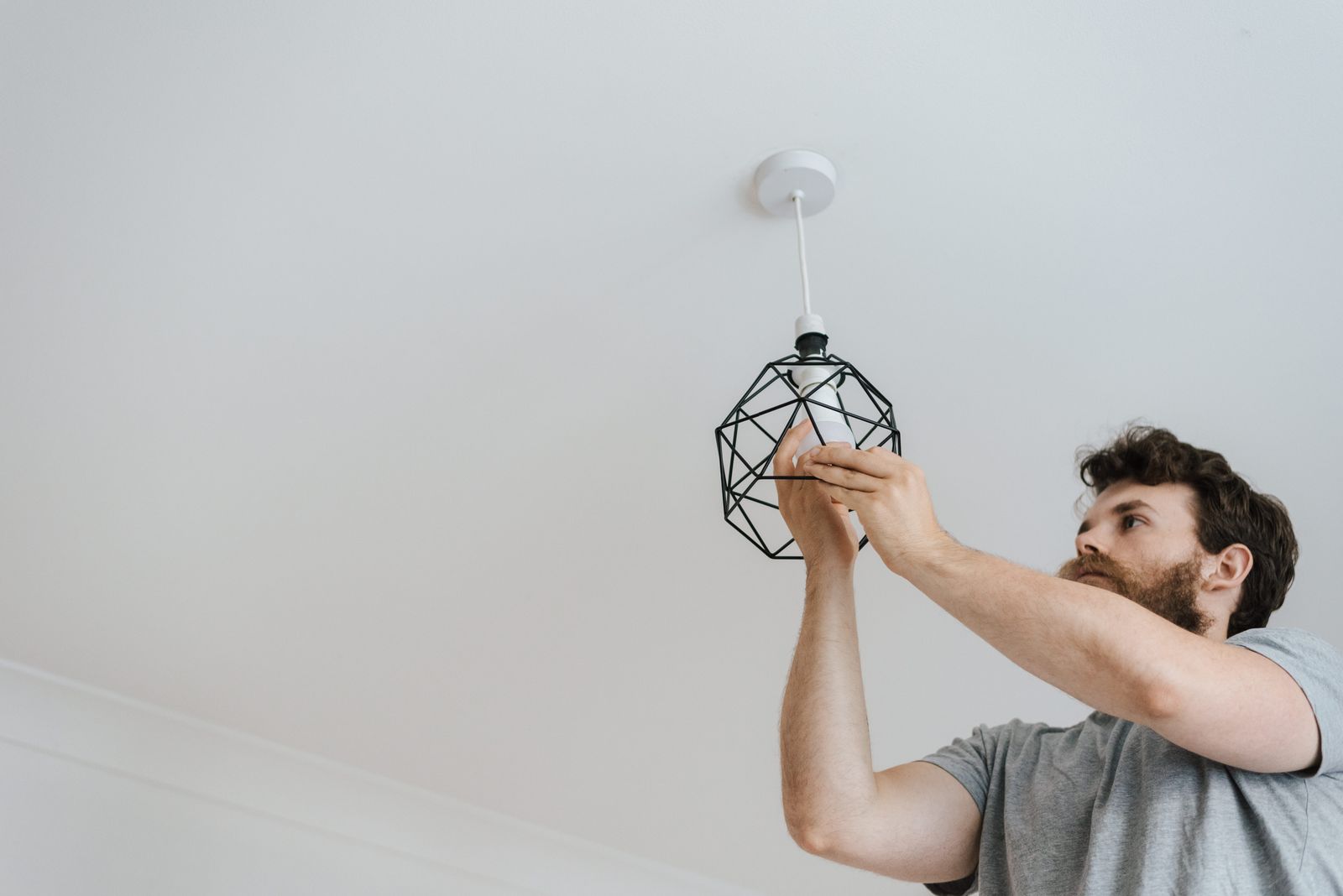 An electrician on a ladder wires a ceiling fixture.
