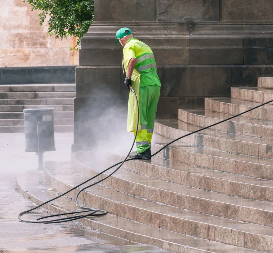 A power washer in work gear cleans a set of stone steps