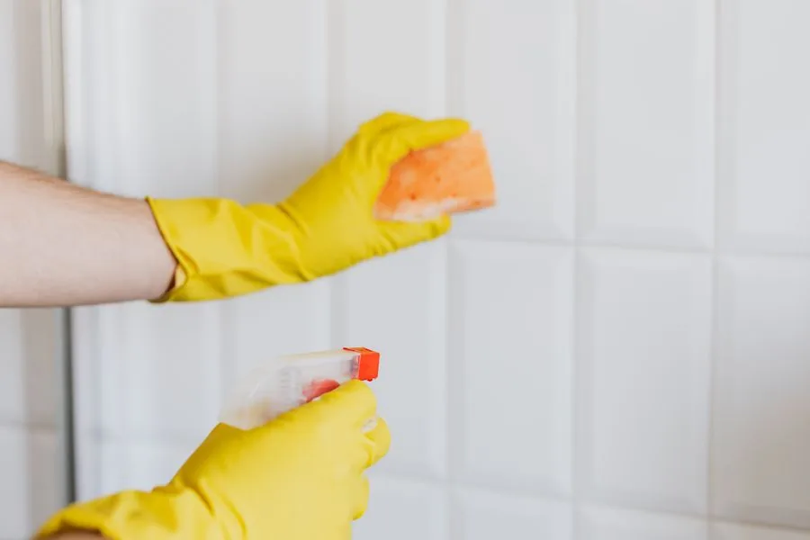 A cleaner in rubber gloves scrubbing tiles during a deep clean