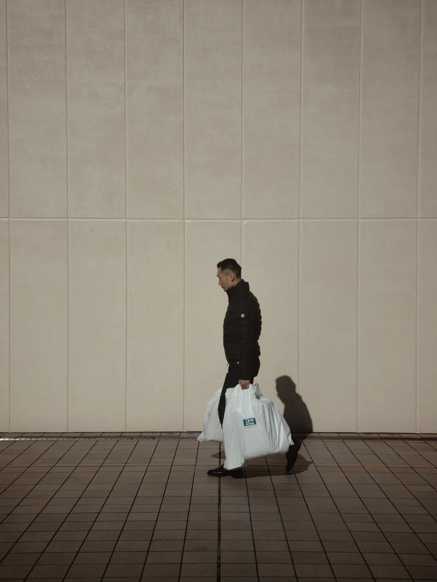 A person walking along the sidewalk carrying shopping bags from a few errands