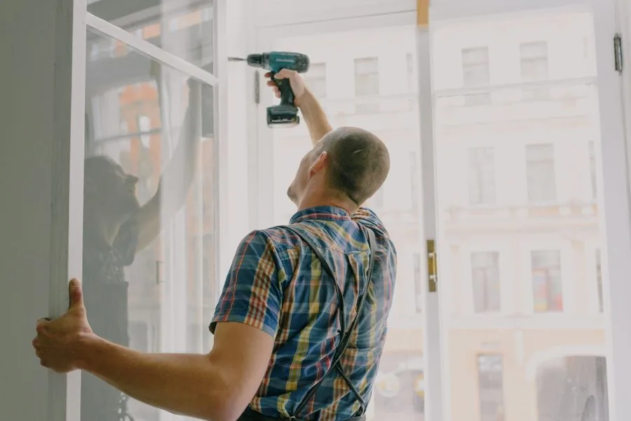 A handyman using a drill to install a window frame inside a home