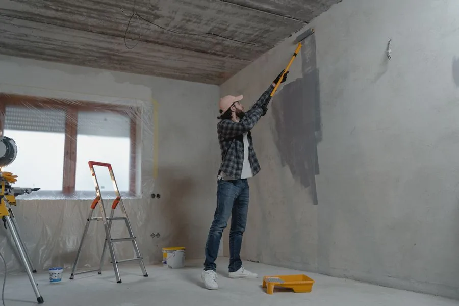 A painter on a stepladder rolls fresh paint onto an interior wall