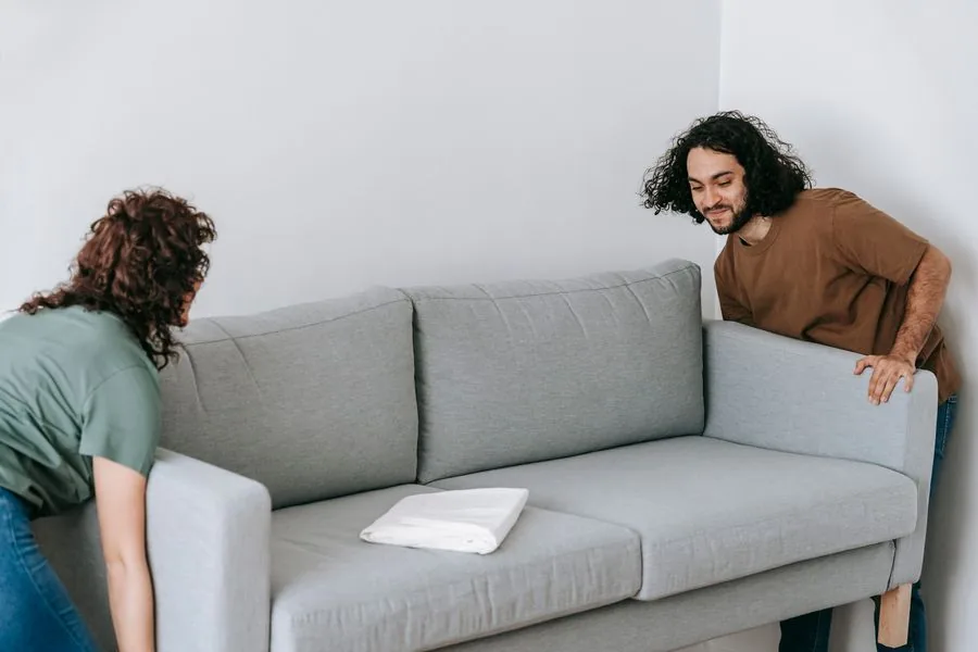 Two people sliding a sofa into place inside a living room