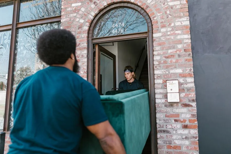 Two movers carrying a heavy couch through a doorway
