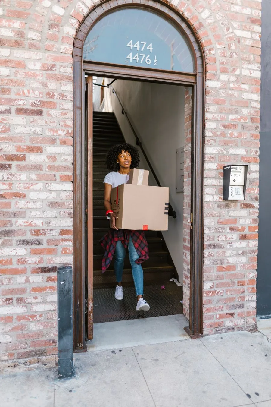 A mover carrying boxes at an apartment building entrance with stairs