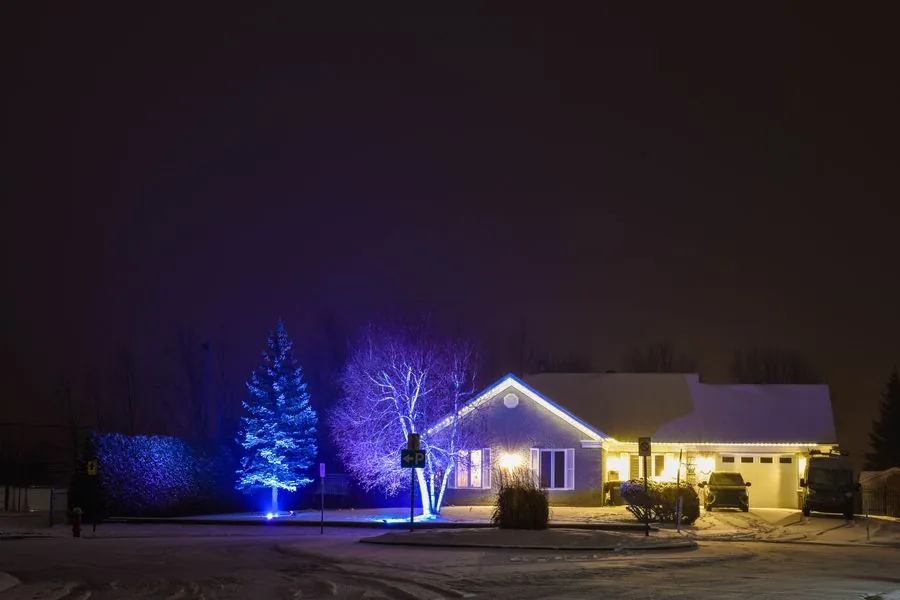 A cozy home exterior decorated with holiday lights on a snowy night