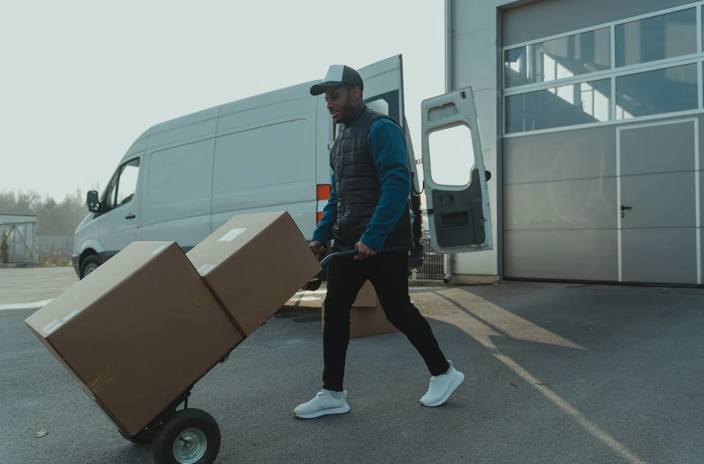 Courier wheeling a hand truck of parcels to a delivery van